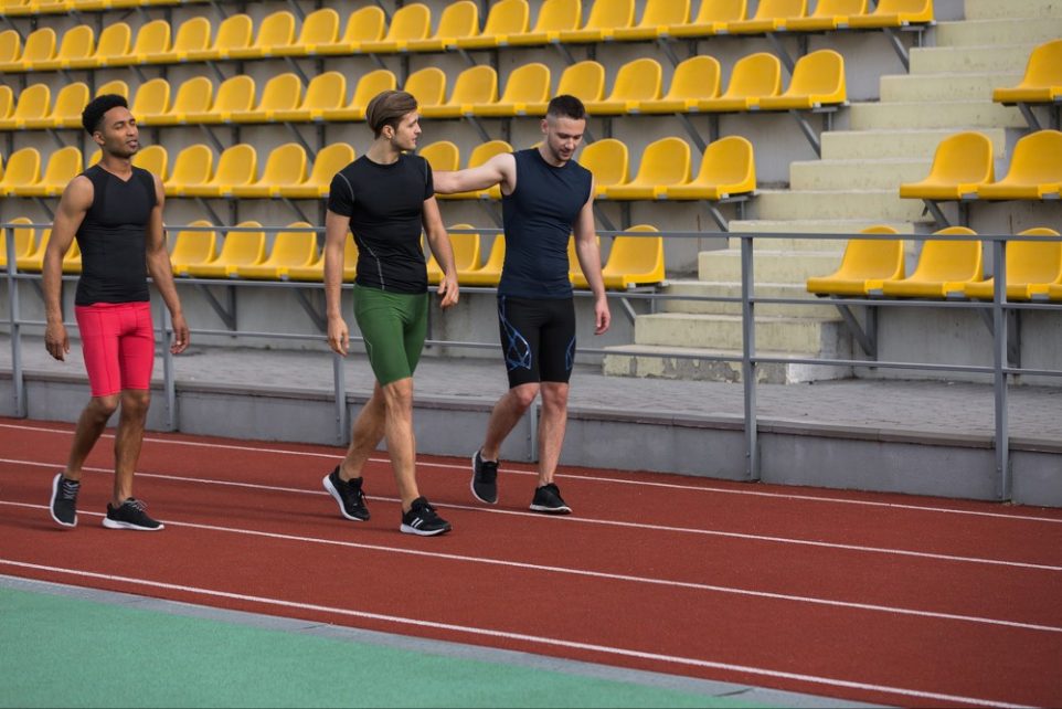 Three college guys walking on the track, embodying the essence of teamwork and endurance after a run, highlighting the unseen but important role of electrolyte powder in their recovery strategy.