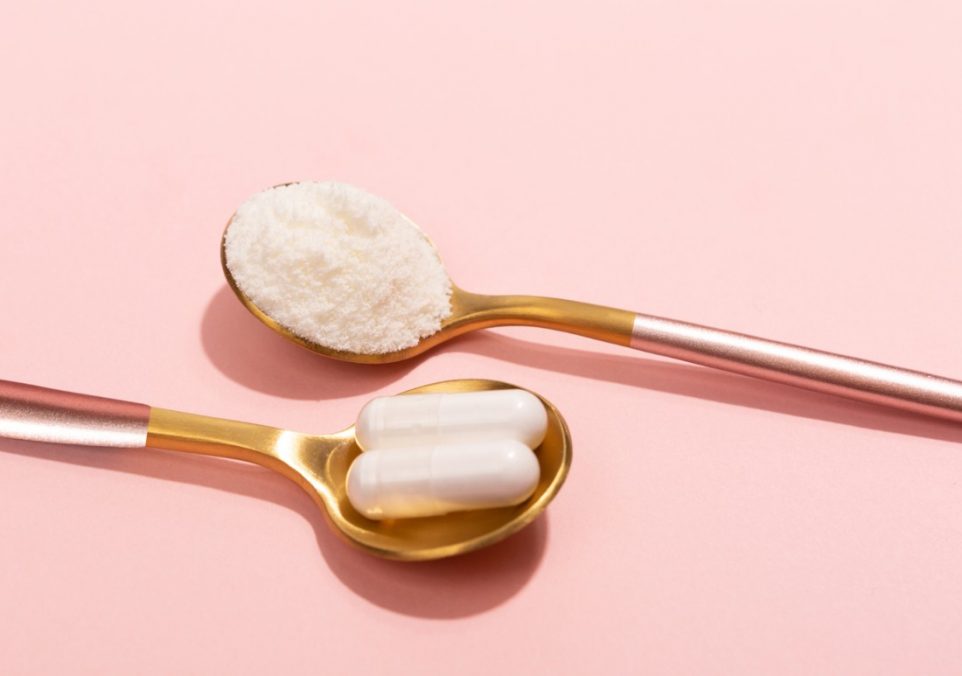 Two teaspoons on a pink background, one holding collagen supplement powder and the other holding two collagen capsules.