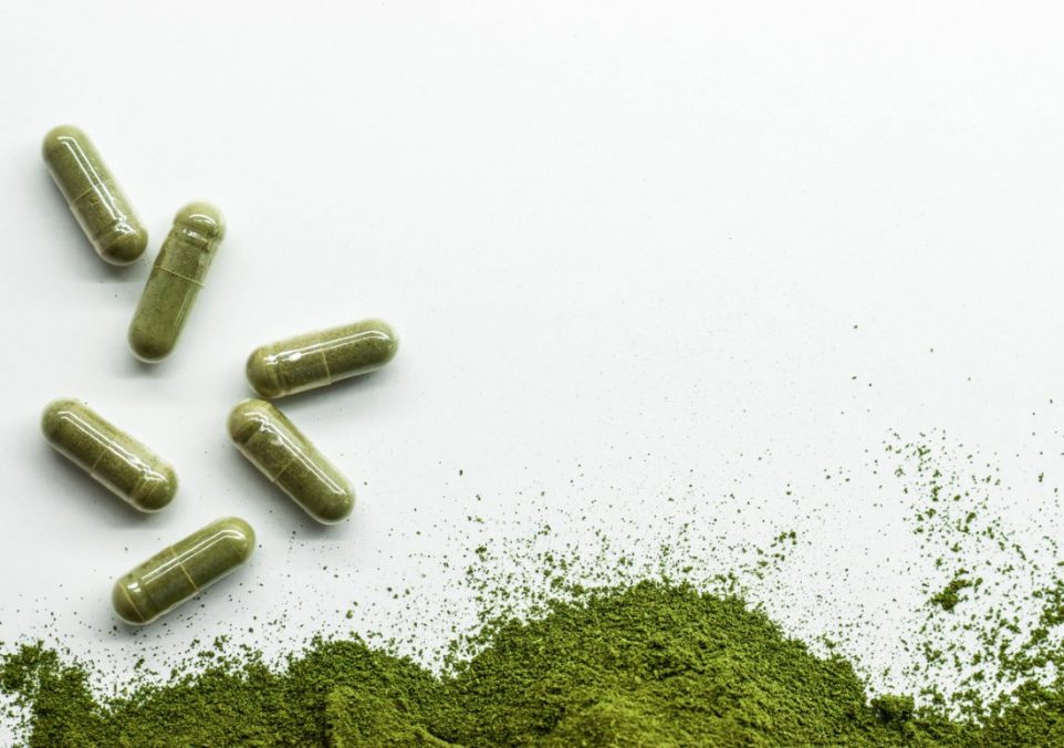 Six green tea extract capsules and green tea extract powder on a plain white background.