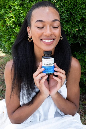 A beautiful woman smiling and holding a bottle of the Live Conscious Collagen Supplement.